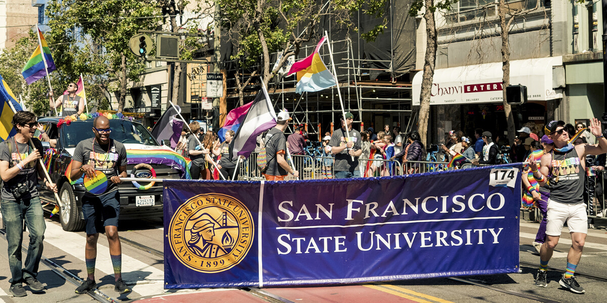 Photo of students, faculty and staff carrying a San Francisco State University banner while marching in 2019 Pride Parade